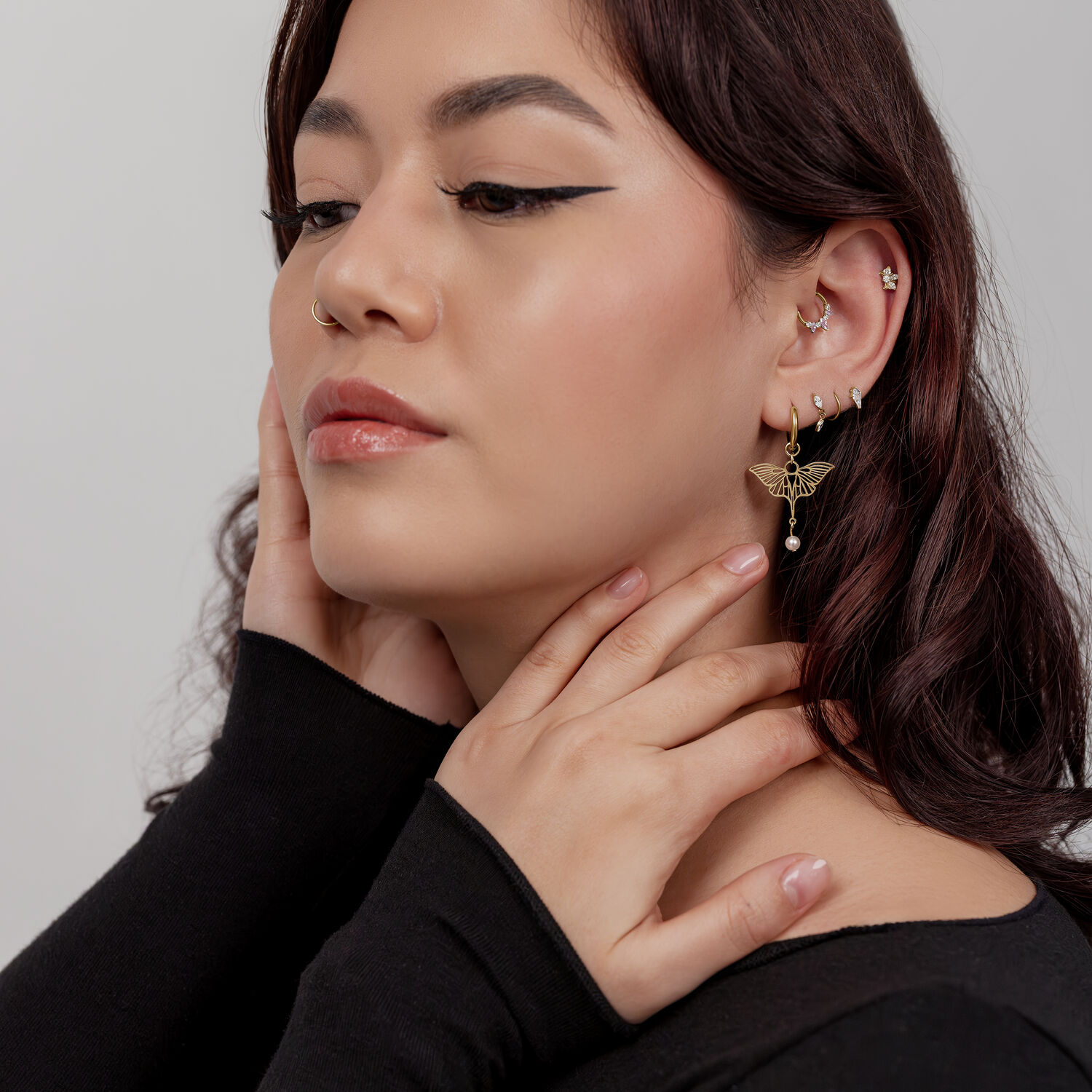 Mujer con pendientes de libélula dorados, camiseta negra, pared blanca