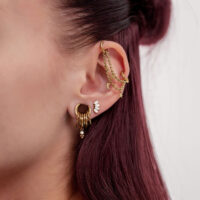 Cadena de piercing dorada con luna y estrellas en una oreja con varios aros dorados