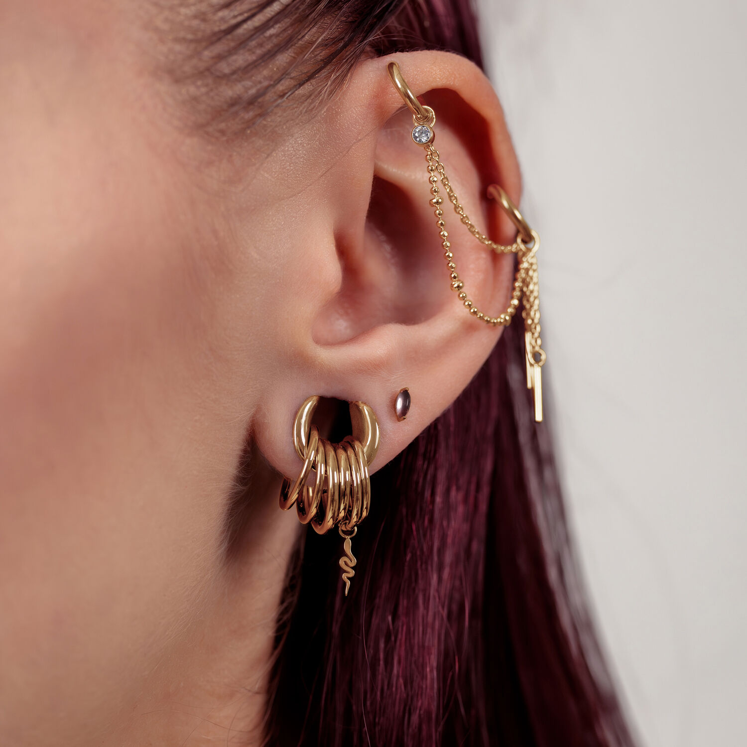 Cadena de piercing dorada, 25 mm de longitud, llevada en la oreja sobre fondo neutro