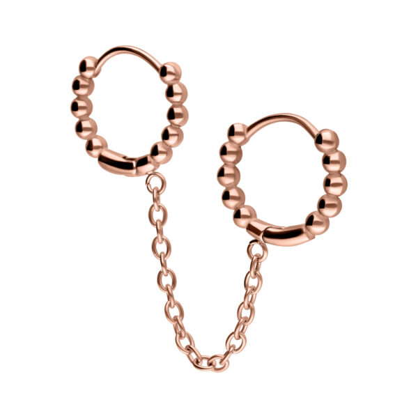 Aros Doble Huggie en oro rosa con diseño de bolas, conectados por una cadena sobre fondo blanco