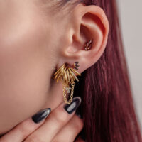 Piercing dorado con colgante de cristal en la oreja, pelo rojo