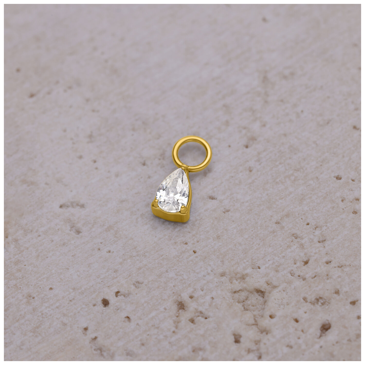 Colgante de piercing dorado con gota de cristal sobre fondo claro