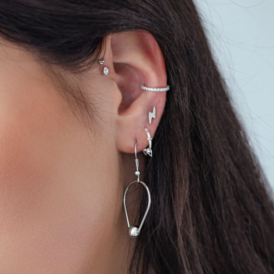 Primer plano de una oreja con varios piercings plateados, incluido uno con cristal