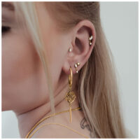 Primer plano de una oreja con varios piercings dorados, incluido un Push Fit Crystal Star Labret de 9,0 mm de longitud.