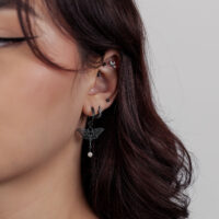 Primer plano de una oreja con varios piercings negros, incluyendo un accesorio de loto con un pequeño colgante.