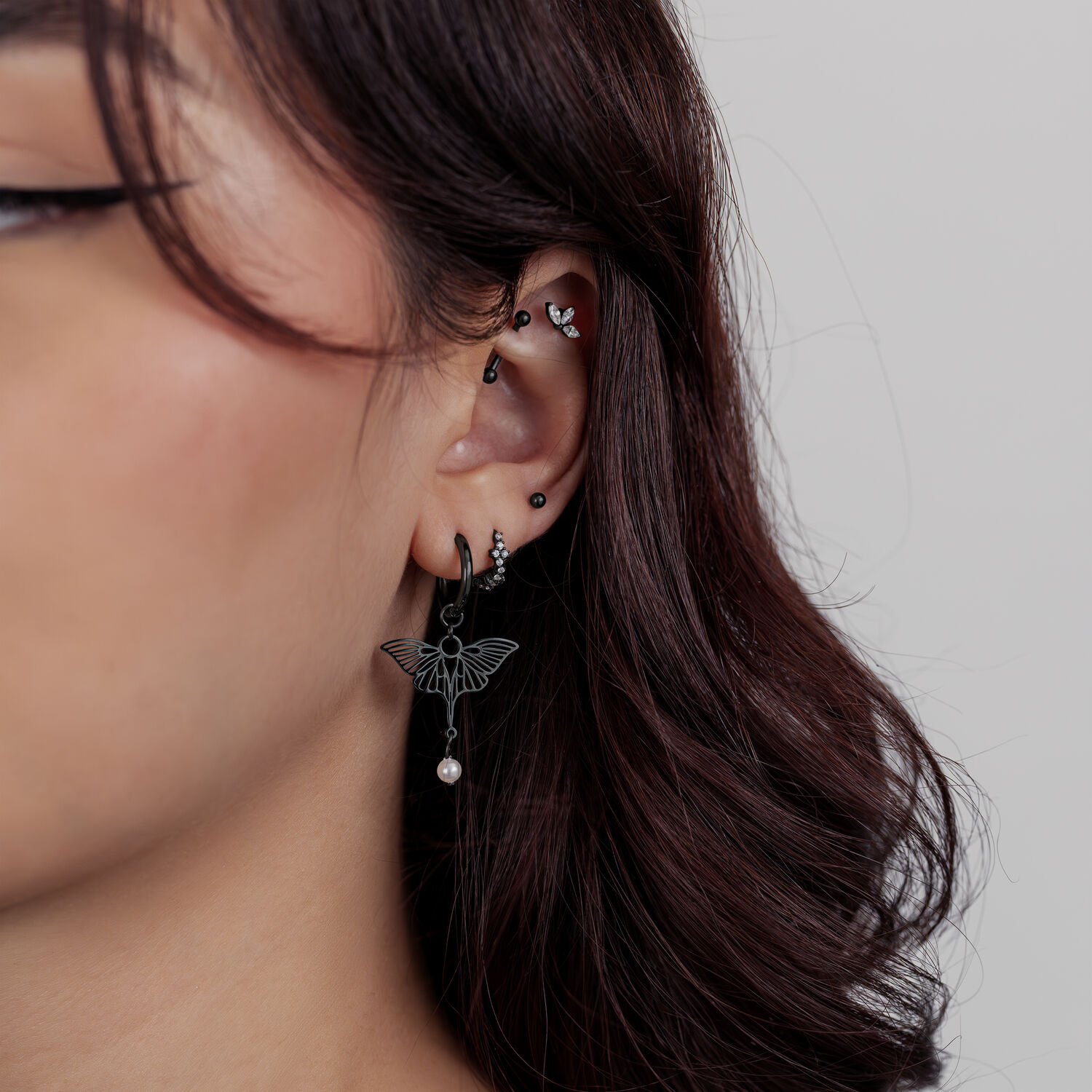 Primer plano de una oreja con varios piercings negros, incluyendo un accesorio de loto con un pequeño colgante.