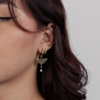 Piercings de oro con colgante de mariposa Primer plano de una oreja con piercings dorados y colgante de mariposa, fondo blanco