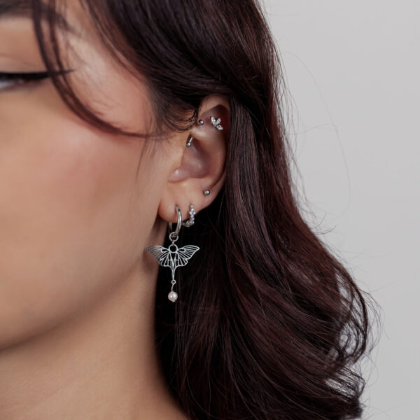 Mujer con varios piercings de oreja plateados y un colgante de mariposa sobre fondo claro