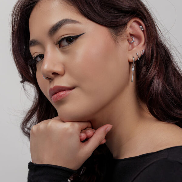 Mujer con piercings plateados, incluyendo una hoja de cristal, sobre fondo gris