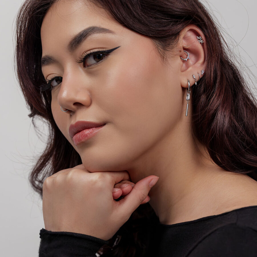Mujer con piercings plateados, incluyendo una hoja de cristal, sobre fondo gris