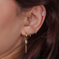 Primer plano de una oreja con varios piercings de cristal dorado en diferentes posiciones