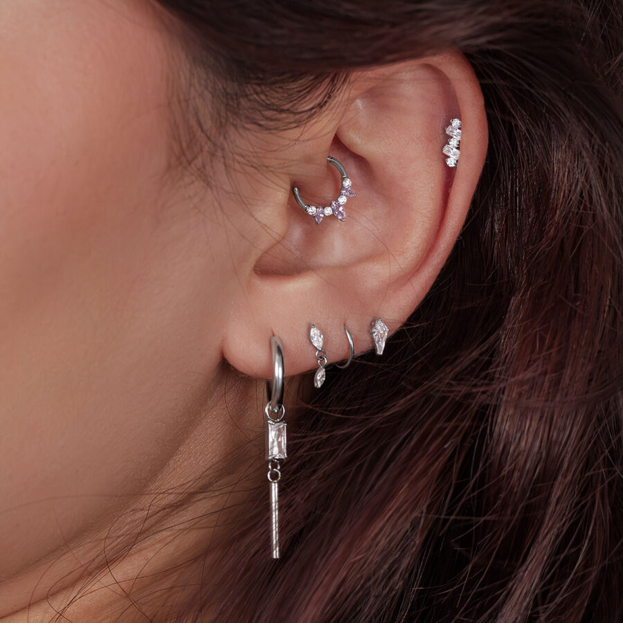 Primer plano de una oreja con varios piercings de plata, algunos adornados con cristales