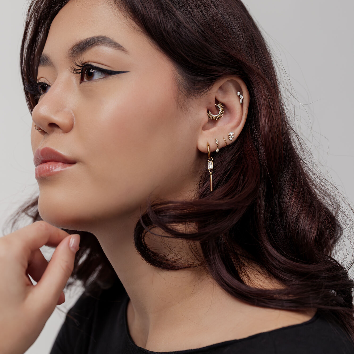 Clicker de Septum Sun Beams Dorado Mujer con varios piercings dorados, incluido un Clicker de Septum Sun Beams, perfil lateral sobre fondo gris