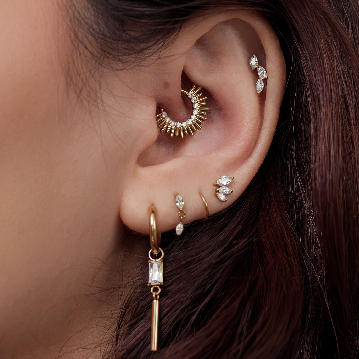 Goldener Sun Beams Septum Clicker Oreja con varios piercings dorados, incluyendo un Sun Beams Clicker, frente a cabello castaño