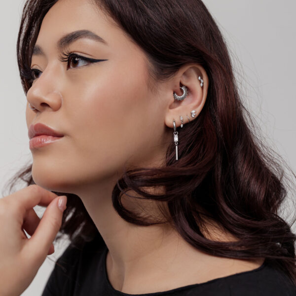 Mujer con varios piercings de plata en orejas y nariz, clicker de septum en forma de rayos de sol