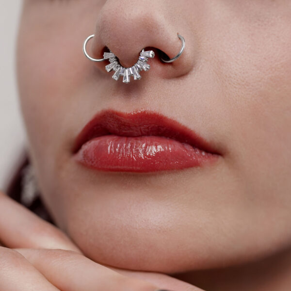 Primer plano de un clicker de septum plateado con cristales en una nariz, labios rojos visibles