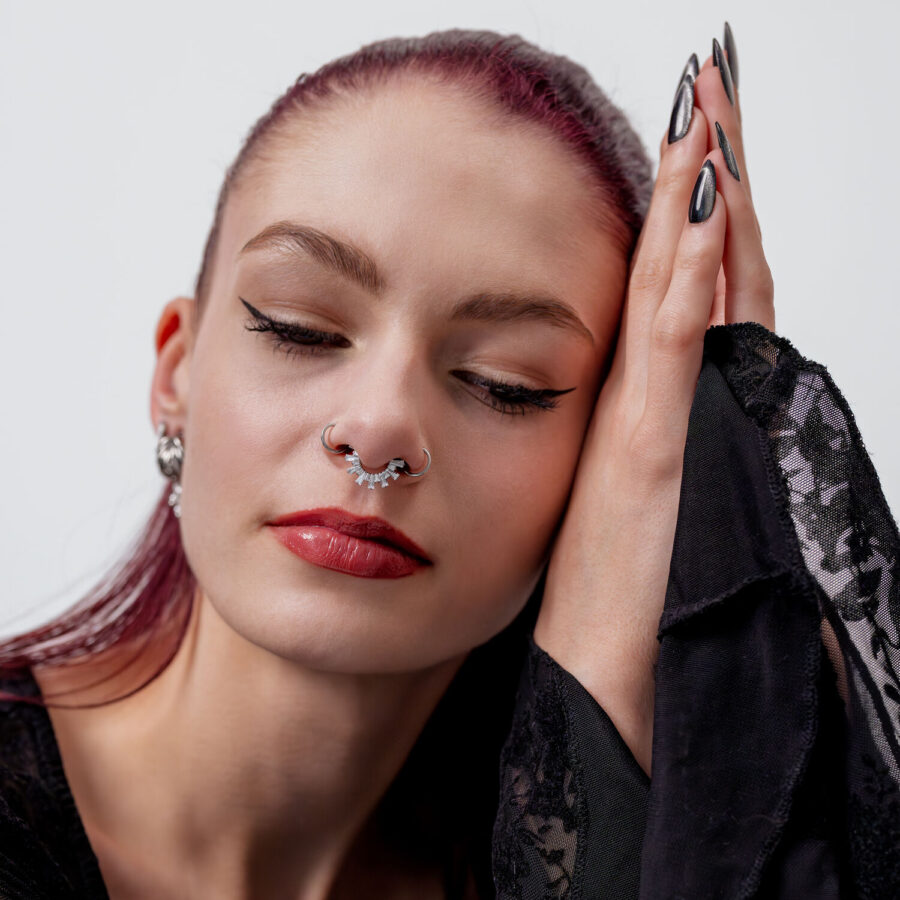 Mujer con ojos cerrados, lleva un clicker de septum de cristal plateado, ropa negra