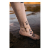 Tobillera dorada con colgante de Monstera en tobillo tatuado en el agua