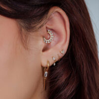 Oreja con varios piercings dorados y con cristales, primer plano
