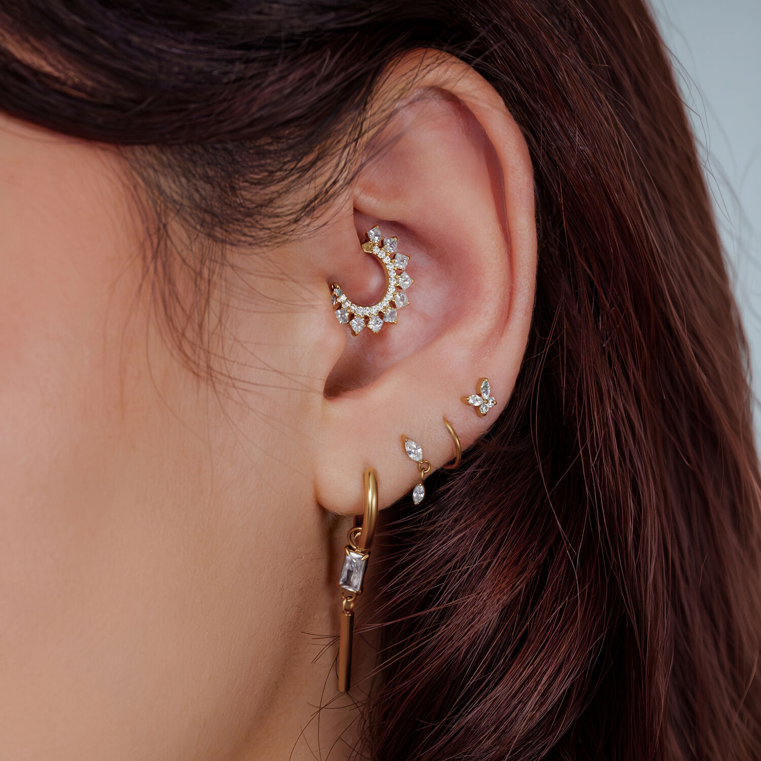Oreja con varios piercings dorados y con cristales, primer plano