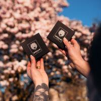 Dos cajas negras con el logo de Wildcat, sostenidas por manos, frente a un árbol en flor de fondo