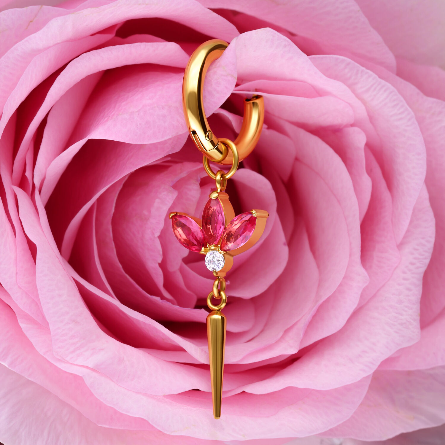 Pendientes dorados con colgante de flor rosa Pendientes dorados con colgante de flor de cristal rosa frente a una rosa