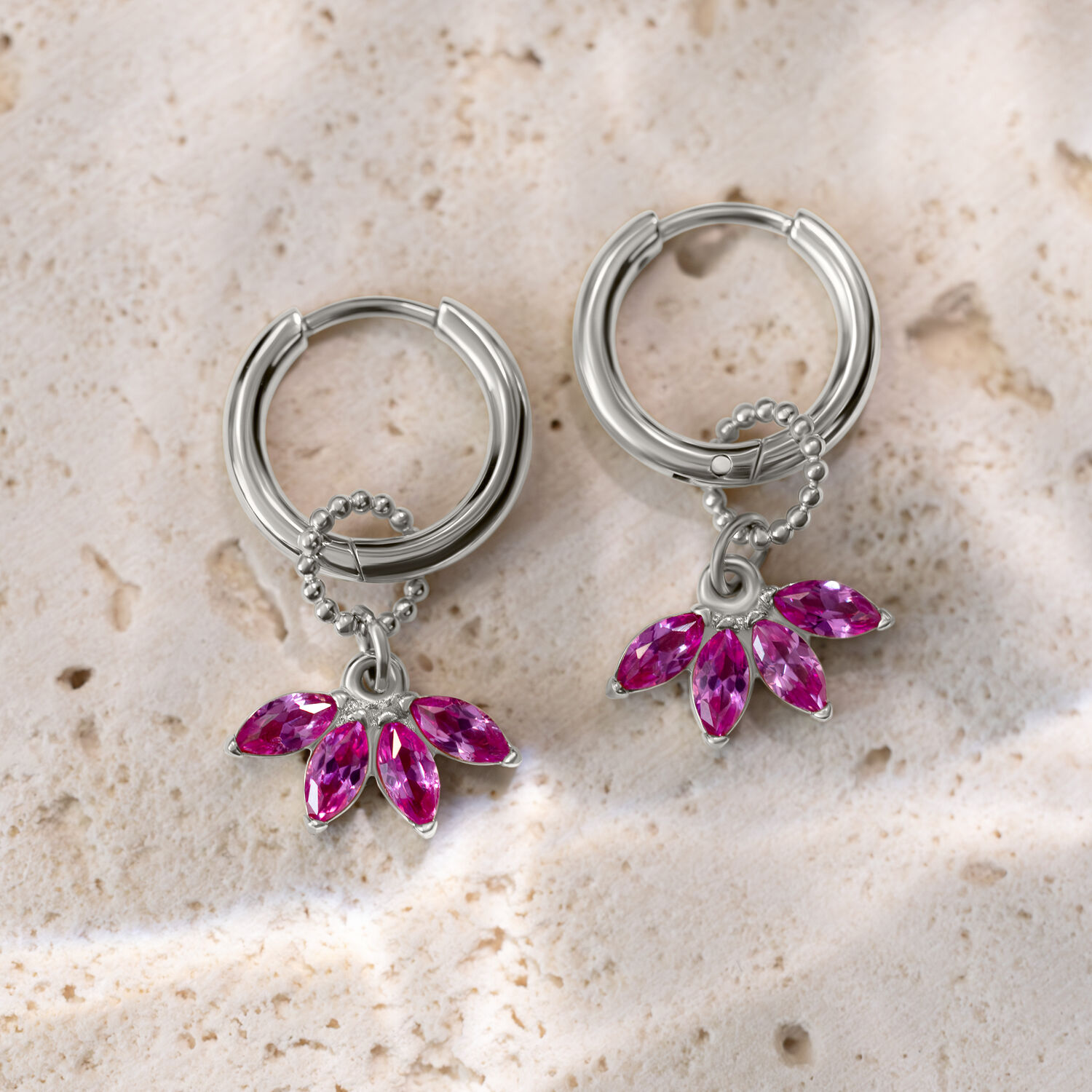 Pendientes de plata con colgantes de cristal rosa sobre superficie de piedra clara