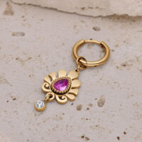 Pendiente dorado con colgante de cristal rosa Pendiente dorado con cristal rosa en forma de gota y pequeño colgante de cristal claro sobre superficie de piedra