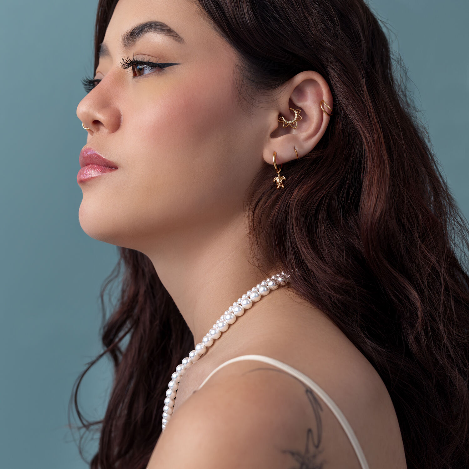 Mujer con aros de tortuga dorados y collar de perlas frente a un fondo azul