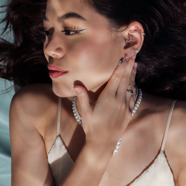 Mujer con pendientes de plata y cadena de perlas, de lado en la luz