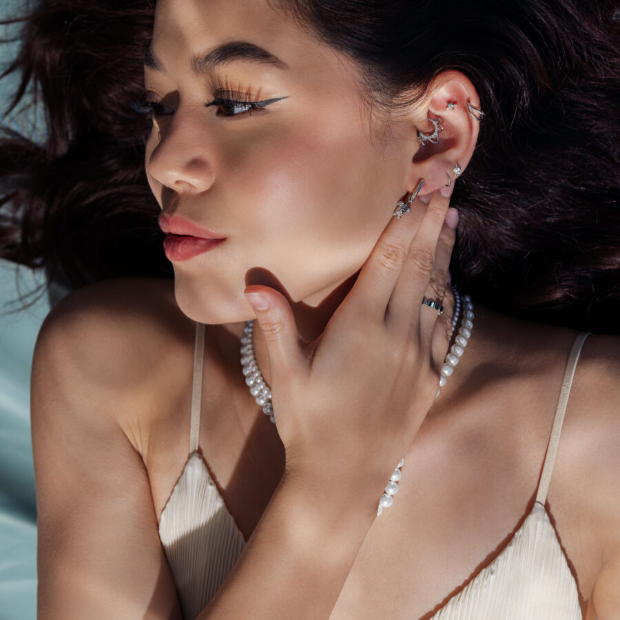 Mujer con pendientes de plata y cadena de perlas, de lado en la luz