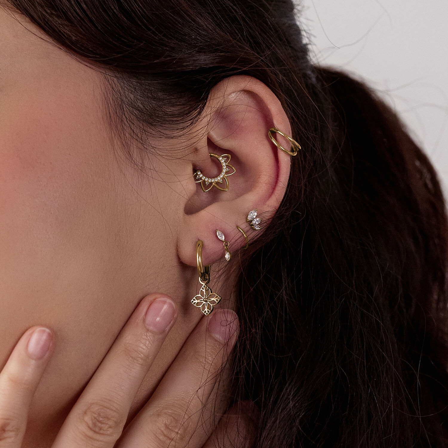 Pendientes dorados con diseño floral Pendientes dorados en oreja con varios piercings, primer plano