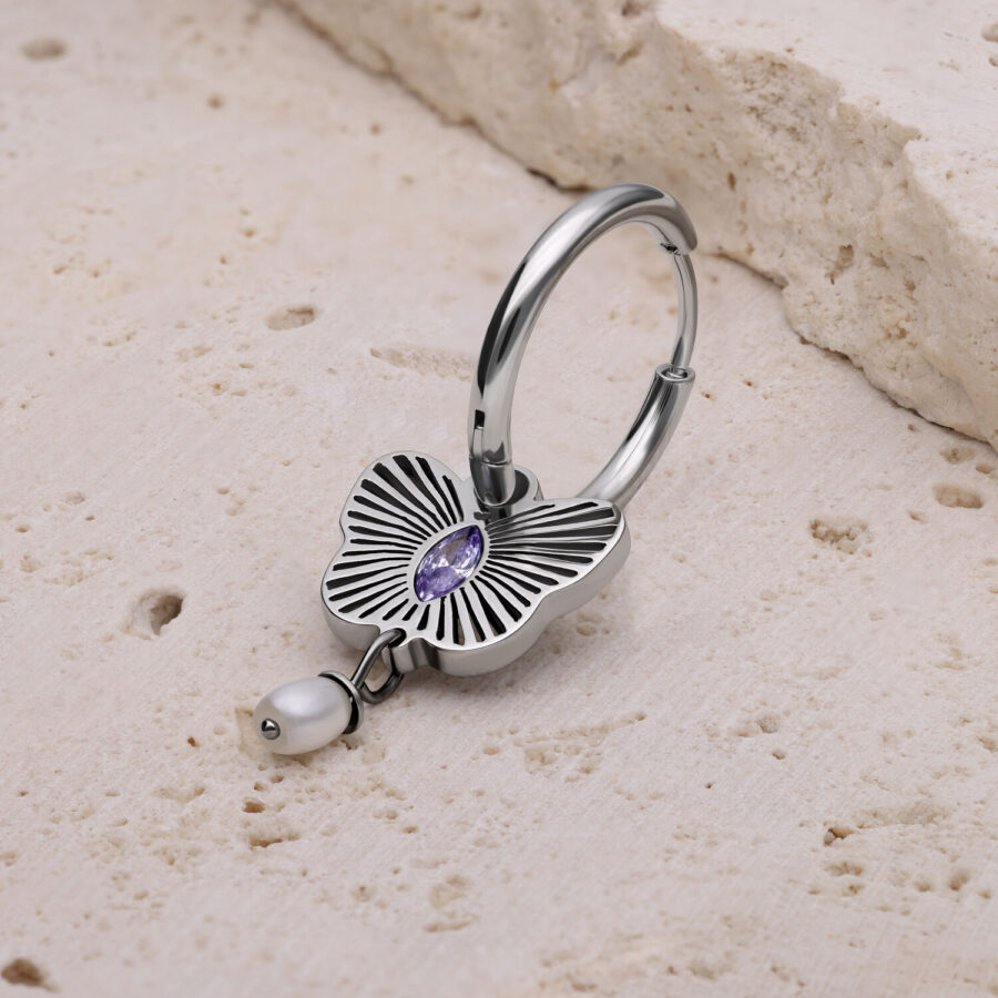Aro de plata con ornamento floral y cristal lavanda sobre piedra clara