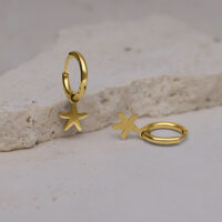 Mini aros dorados con estrella de mar Zlata Dos aros dorados con colgantes de estrella de mar sobre una superficie de piedra