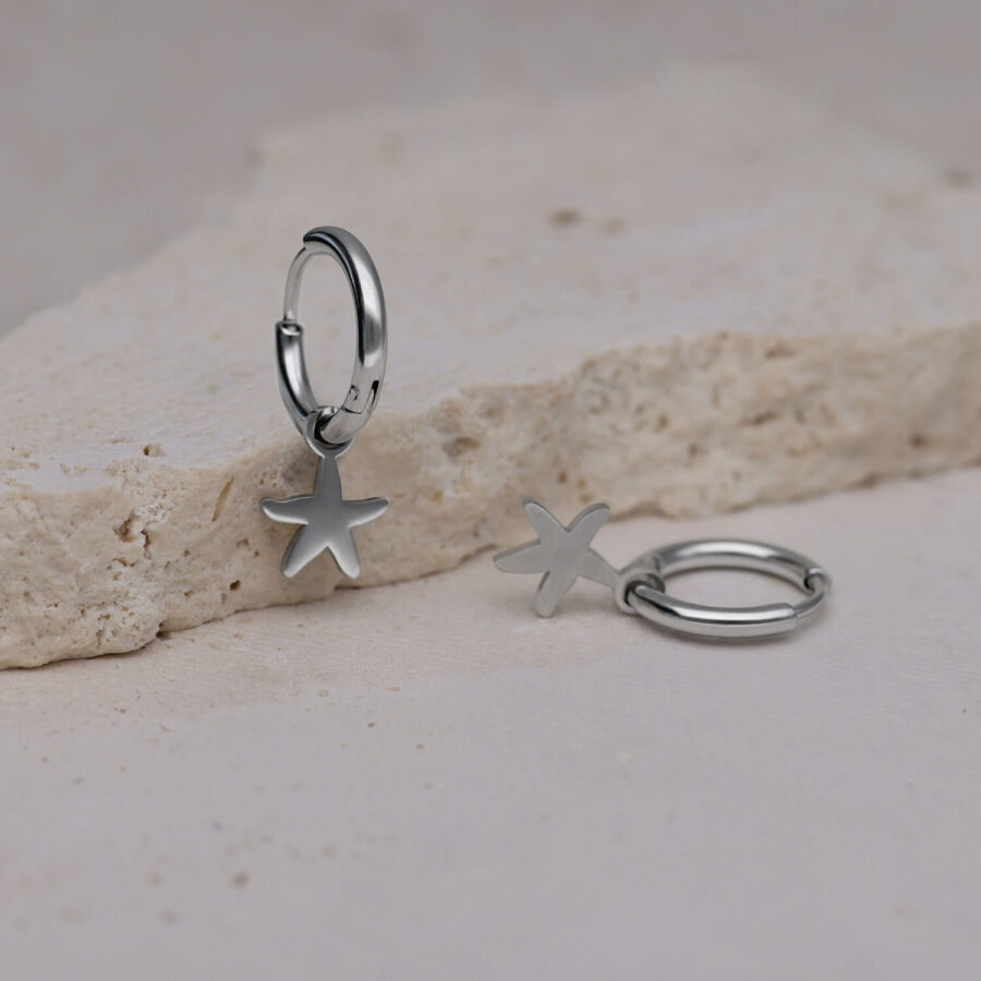 Dos aros plateados con colgante de estrella de mar sobre piedra clara
