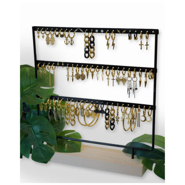 Soporte de metal negro con pendientes sobre base de madera, rodeado de hojas verdes