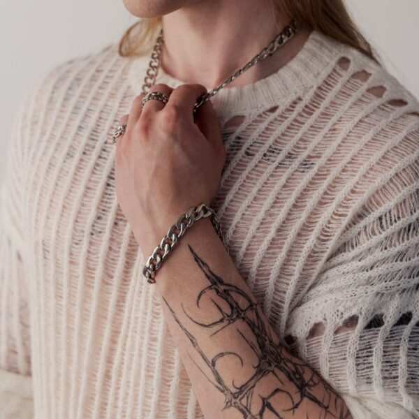 Persona con brazo tatuado lleva una pulsera Chunky plateada y un suéter tejido