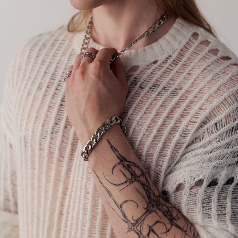 Persona con brazo tatuado lleva una pulsera Chunky plateada y un suéter tejido