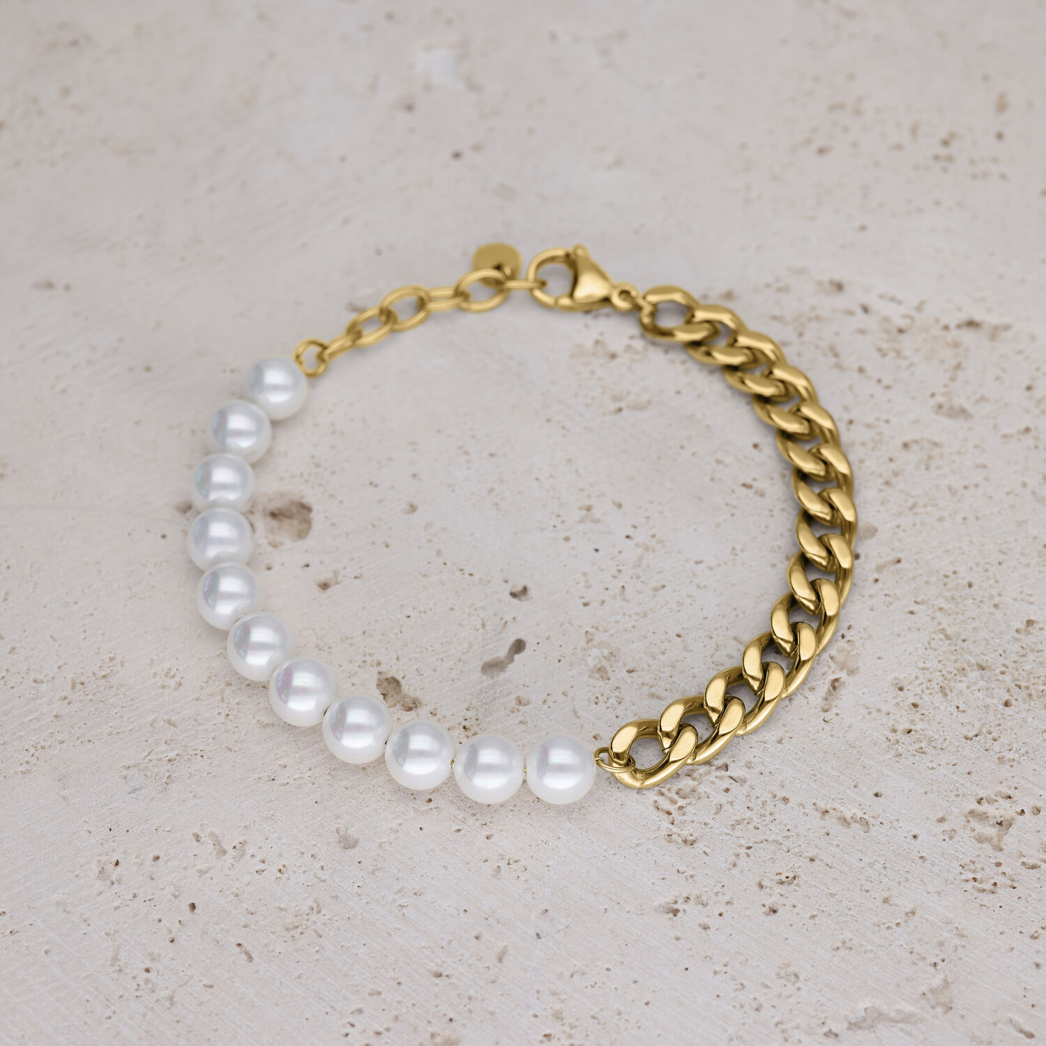 Pulsera con perlas sintéticas blancas y cadena de eslabones dorada sobre fondo beige