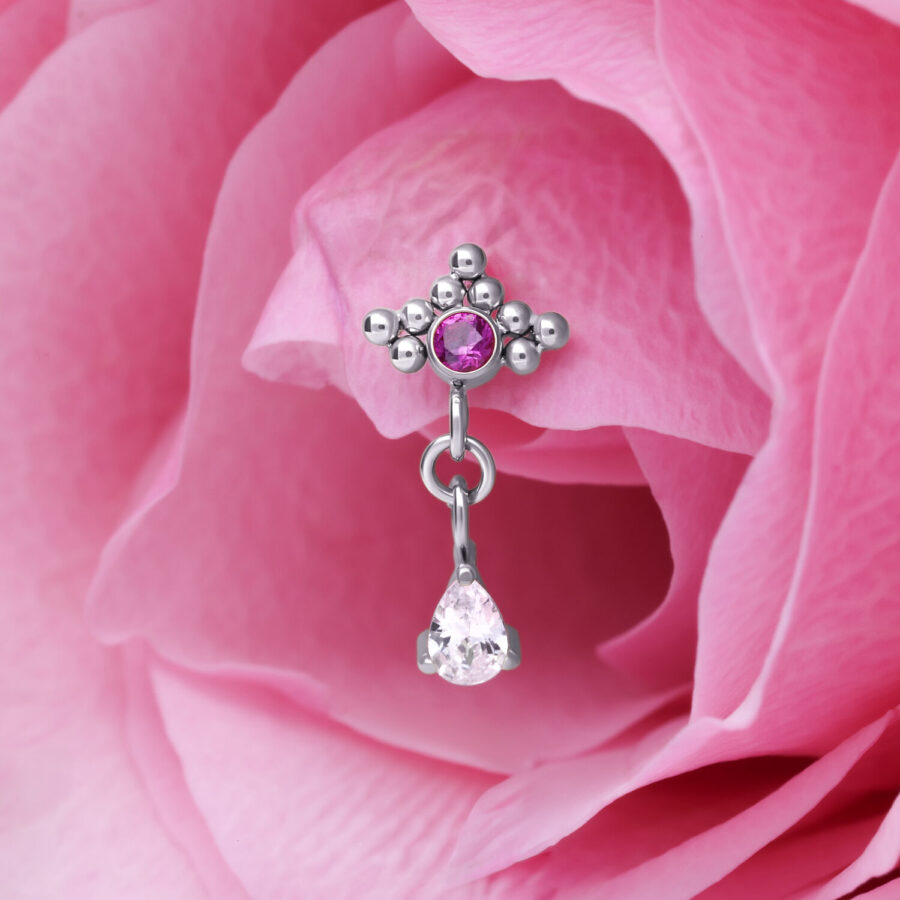 Colgante de piercing plateado con cristal rojo y forma de gota frente a pétalo rosa