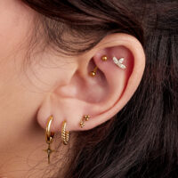 Oreja con varios piercings dorados, incluyendo un accesorio brillante de tres hojas