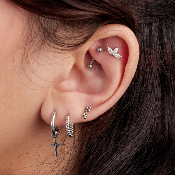 Primer plano de una oreja con varios piercings, incluyendo un colgante de titanio y otras piezas de plata.