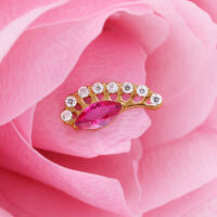 Aplique dorado con cristal rojo ovalado y piedras claras sobre pétalos rosados