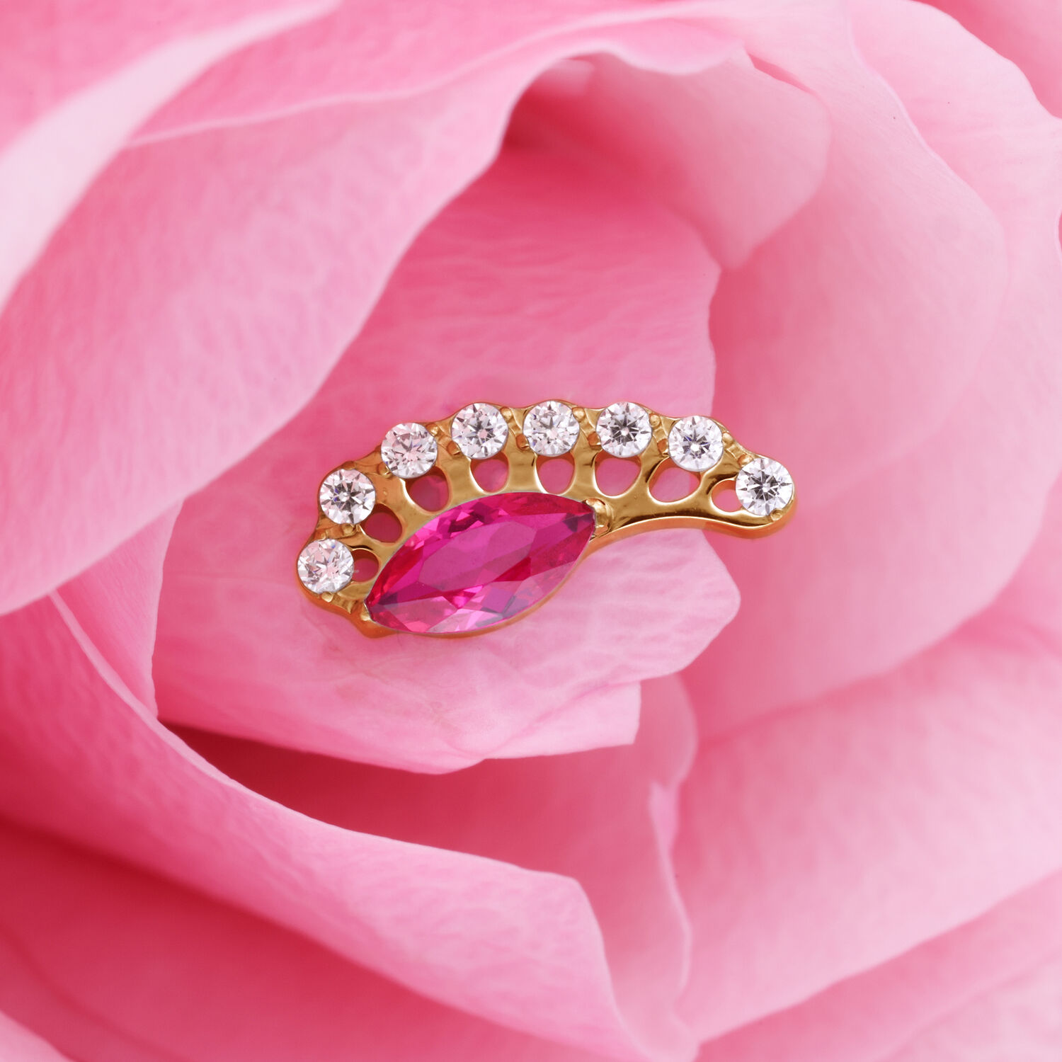 Aplique dorado con cristal rojo ovalado y piedras claras sobre pétalos rosados