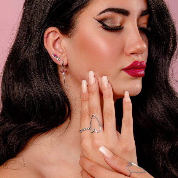 Mujer con pendientes de plata y cristal rojo sobre fondo rosa