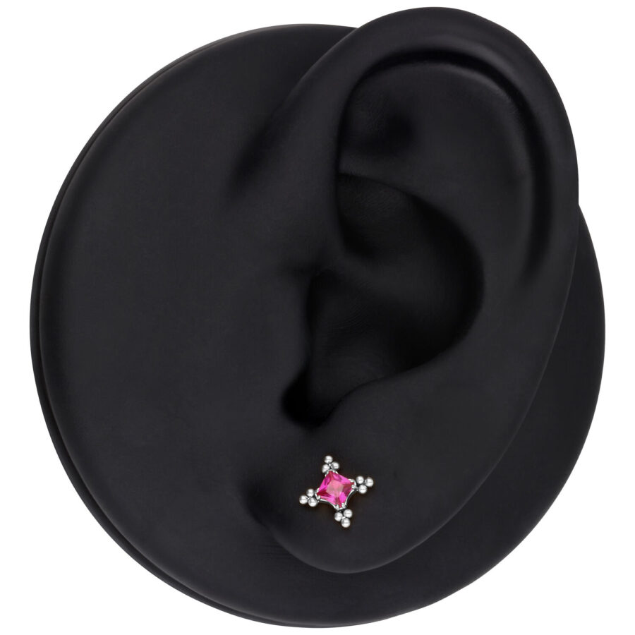Modelo de oreja con accesorio de piercing plateado y cristal rojo sobre fondo negro