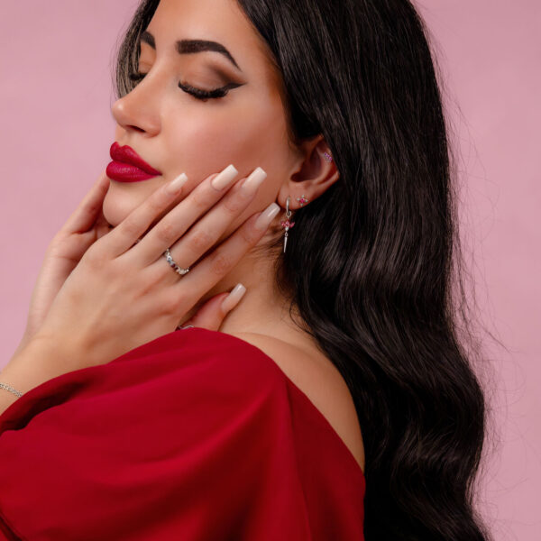 Mujer con labios rojos y cabello largo y liso lleva adorno de plata en la oreja sobre fondo rosa