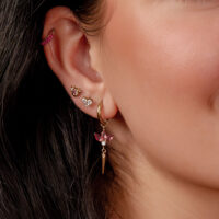 Primer plano de una oreja con varios pendientes dorados, incluido un colgante largo con cristal rosa.