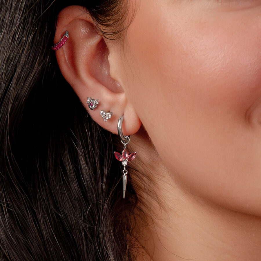 Primer plano de una oreja con varios pendientes de plata y cristales rojos, cabello oscuro de fondo
