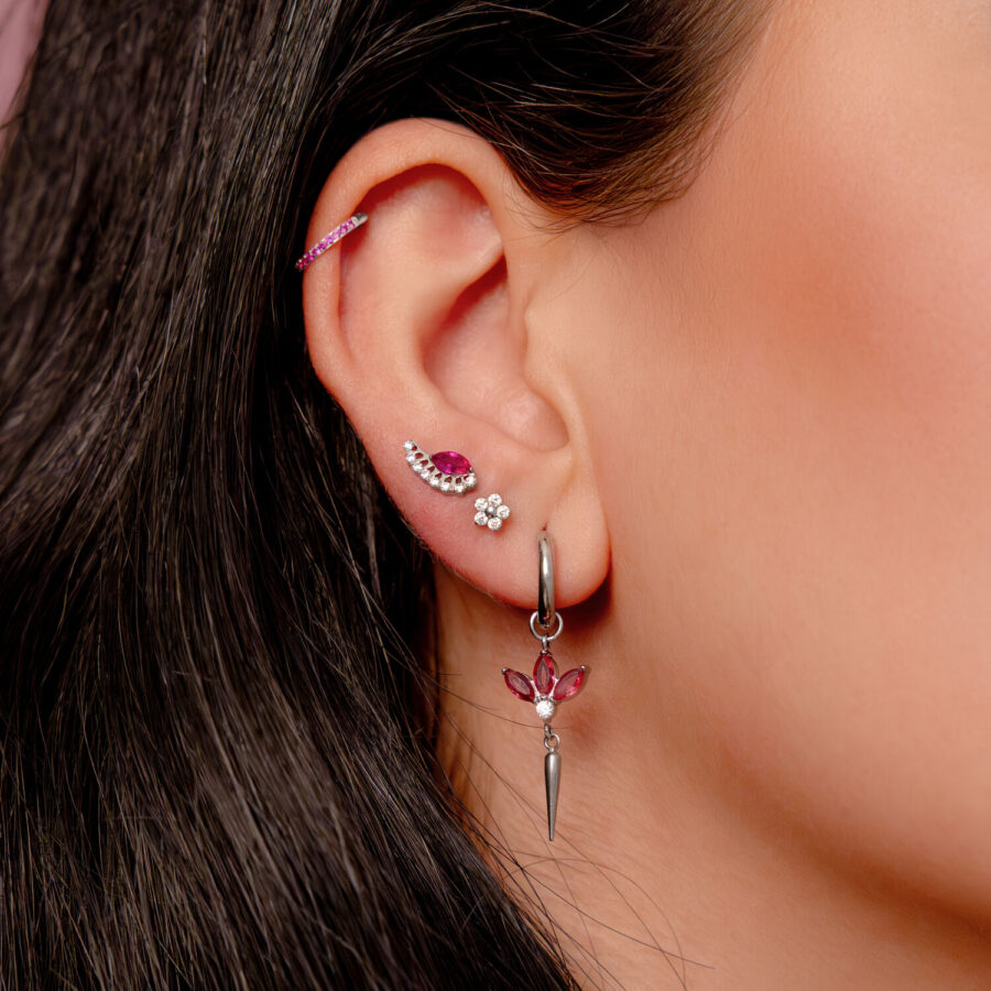 Pendiente de plata en la oreja con cristales rojos y varios piercings en una oreja